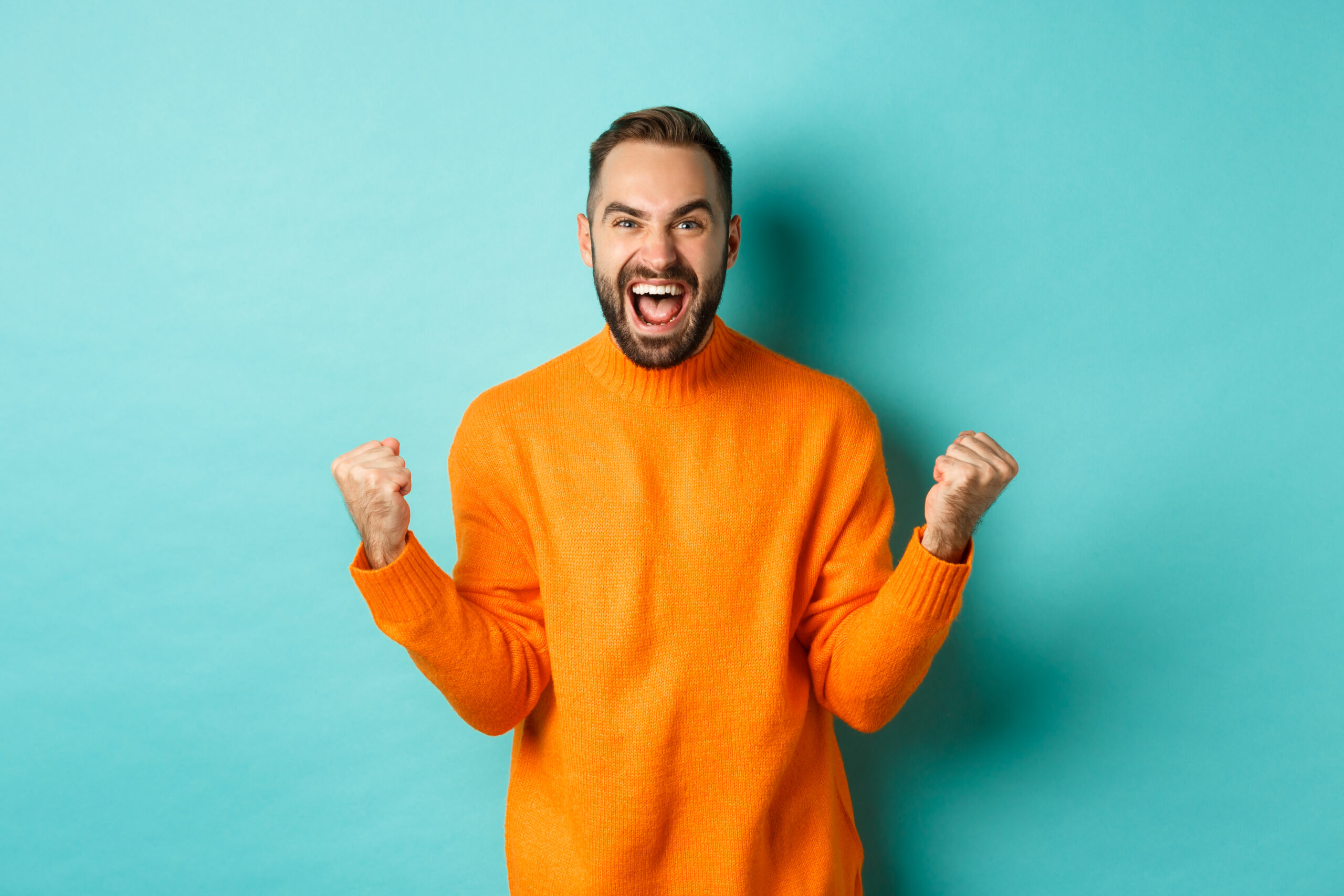 Excited man celebrating victory, rejoicing and making fist pump gesture, winning and looking satisfied, saying yes, achieve goal, standing over light blue background